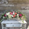 Long floral arrangement of pink, coral, and white roses in a white container