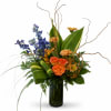 Orange roses and blue flowers in a tall glass vase with curly branches