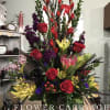 Tall mixed floral arrangement with red roses, purple blooms, and yellow flowers in a dark container