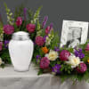 Funeral urn surrounded by purple, white, and orange flowers with a framed portrait