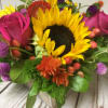 Low wood box arrangement with a sunflower, pink roses, and bright mixed flowers.