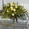 White rose casket spray with cascading greenery on a silver casket