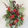Tall standing spray of red gerbera daisies and roses with dramatic greenery on an easel.