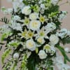 White floral standing spray with roses and lilies on a black easel