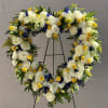 Heart-shaped floral wreath with white roses, yellow blooms, and blue accents on a stand