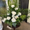 Tall arrangement of white roses with large green tropical leaves on a wooden pedestal.
