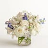 White rose bouquet with purple and pale blue flowers in a clear glass vase