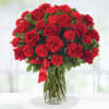 Red roses and carnations arranged in a clear glass vase with a red ribbon
