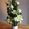 White lilies and roses arranged in a white vase with dark green accents.