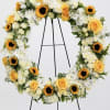 Heart-shaped floral wreath with yellow roses, white flowers, and sunflowers on an easel