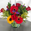 Mixed bouquet of red roses, gerbera daisies, and sunflowers in a glass vase