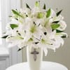 White lilies arranged in a tall vase with a cross emblem