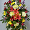 Standing floral spray with red lilies, yellow daisies, and purple accents