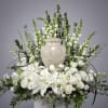 White floral arrangement with lilies and roses around a stone urn