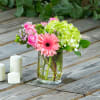 Pink roses and a gerbera daisy in a glass vase with candles nearby