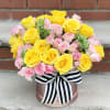 Yellow and pink rose bouquet in a round box with a striped ribbon