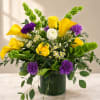 Bouquet of yellow roses, purple carnations, and white daisies in a glass vase