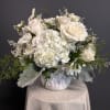 Low white arrangement of roses and hydrangeas in a white ceramic pot on a draped pedestal
