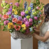 A tall, joyful mixed flower arrangement in a white wicker basket -
