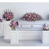 Multiple pink and purple floral funeral arrangements around a white casket