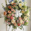 Circular floral wreath with roses, ranunculus, and blue flowers on a stand