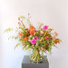Bouquet of orange and pink dahlias with mixed wildflowers and grasses in a clear glass vase.