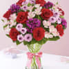 Bouquet of red roses and pink flowers in a glass vase with a pink ribbon