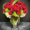 Tall arrangement of red roses with white and green blooms in a clear pedestal glass vase