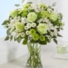 Green and white bouquet of roses, carnations, and daisies in a clear glass vase