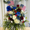 Large patriotic floral arrangement with red, white, and blue roses and flags