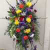 Tall standing floral spray with multicolored blooms and purple ribbon