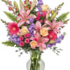 Mixed bouquet of pink lilies, roses, and purple flowers in a glass vase