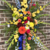 Large standing floral spray with yellow, blue, and mixed blooms on a brick wall