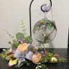 Pastel floral arrangement with roses and purple accents beside a hanging glass ornament