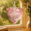 Heart-shaped pink and white glass ornament hanging in a window