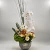 Tall floral arrangement with white orchids and cream roses in a gray vase