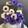Purple and blush anemones arranged in a round white vase
