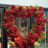 Heart-shaped red rose wreath on a stand with a ribbon bow