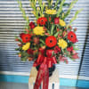 Tall floral arrangement with red roses, gerbera daisies, and yellow blooms in a black vase