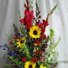 Tall mixed bouquet with sunflowers, red gladiolus, and blue flowers in a white vase