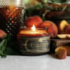 Lit candle in a glass jar surrounded by peaches and fruit slices