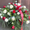 A lush, garden-style casket spray built from abundant red and white roses