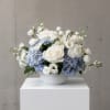 White and pale blue floral arrangement in a white bowl vase