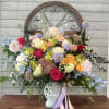 Colorful mixed flower arrangement in a white vase with ribbon tails