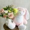 Pink plush bunny beside a vase of pale roses and mixed flowers
