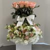 Tall floral arrangement of pink roses and white hydrangeas in a white vase with a ribbon