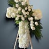White floral cross on an easel with roses and hydrangeas