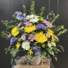 Bright mix of chrysanthemums and daisies arranged in a small sympathy urn
