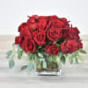 Low arrangement of red roses in a clear glass cube vase with trailing greenery