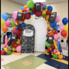 Colorful balloon arch with notebook cutouts and oversized pencils